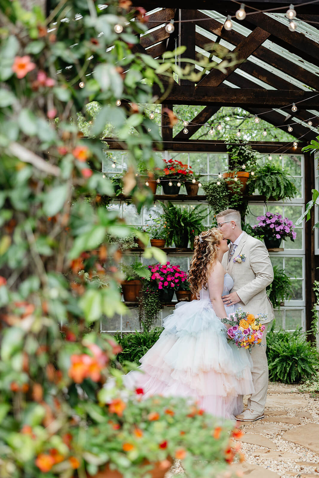 Vaughan Greenhouse Spring Wedding Photography 12 groom kissing bride in a greenhouse filled with pots of flowers, string lights, and greenery growing all around