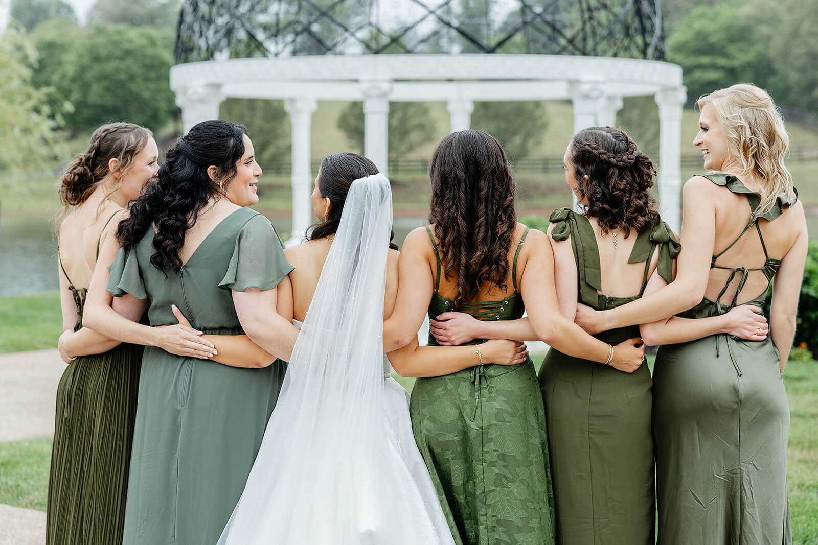 Matt + Adriana's May Wedding Photography 17 bride and bridesmaid standing linked together with their backs facing the camera, all the bridesmaids are wearing different shades of green dresses