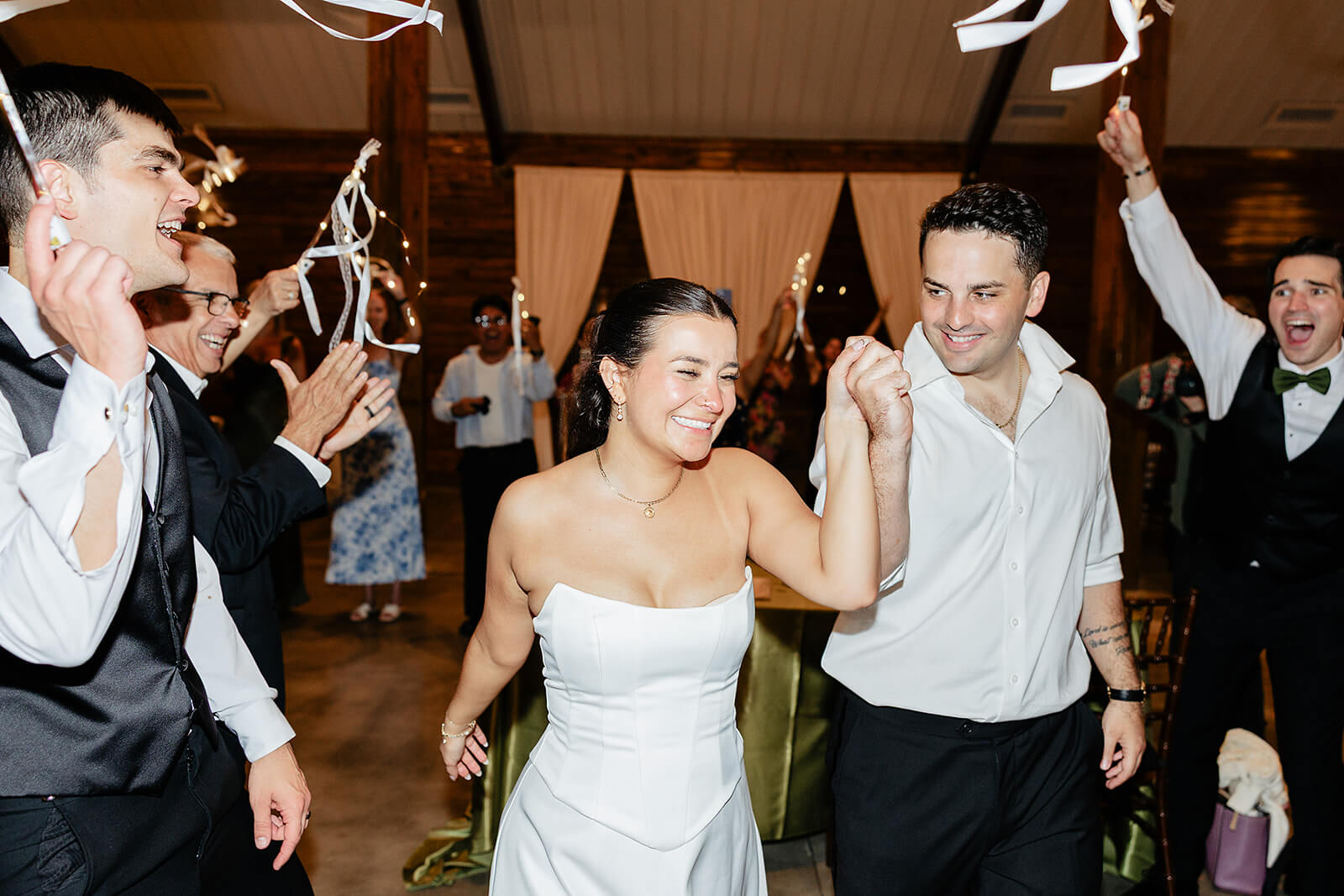 Matt + Adriana's May Wedding Photography 43 bride and groom holding hands and leaving the venue while their guests wave ribbons and cheer at them