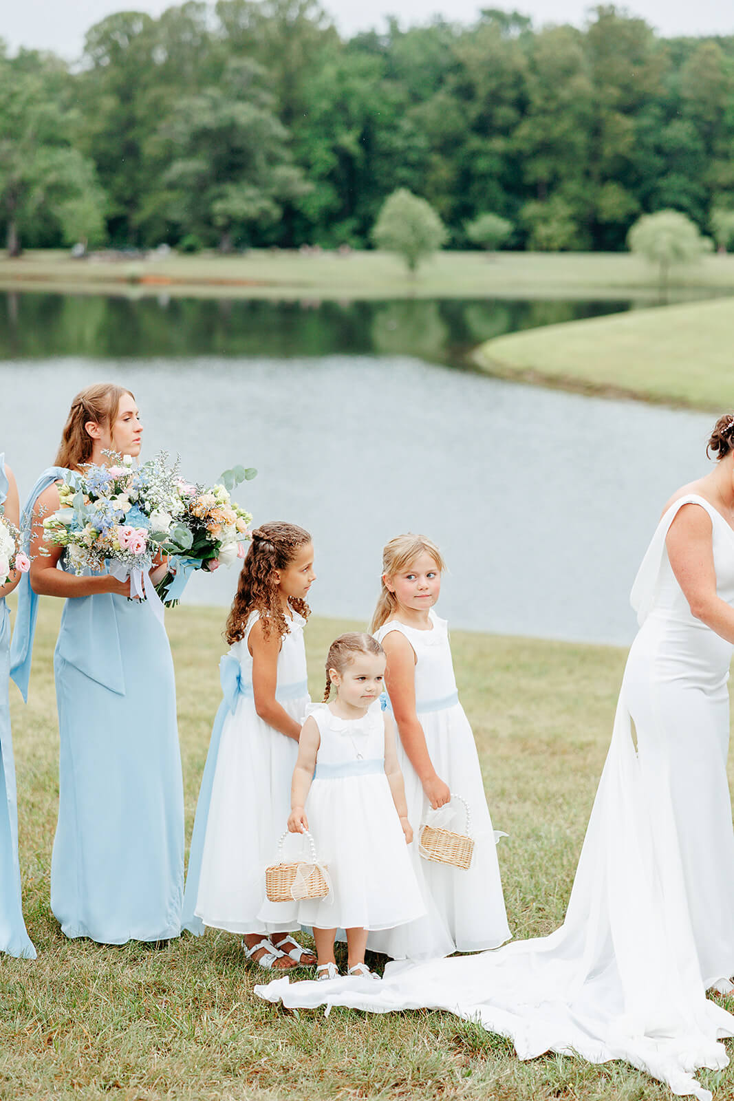 Family Farm Spring Wedding Photography 20 bridesmaids and flower girls standing behind bride on lawn with pond in the background