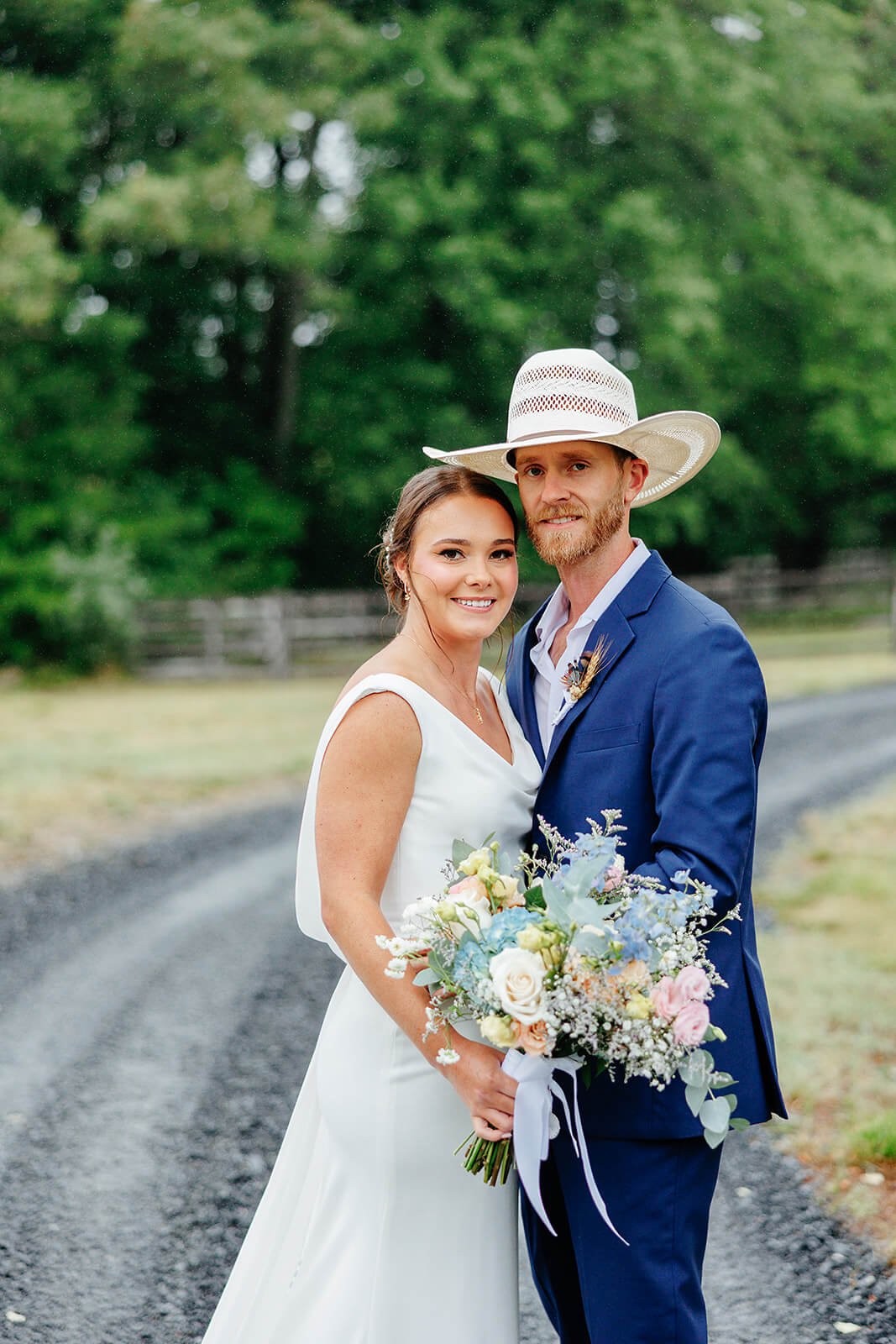 Family Farm Spring Wedding Photography 28 bride and groom facing each other and smiling at the camera, they are standing on a gravel road with lots of trees in the background