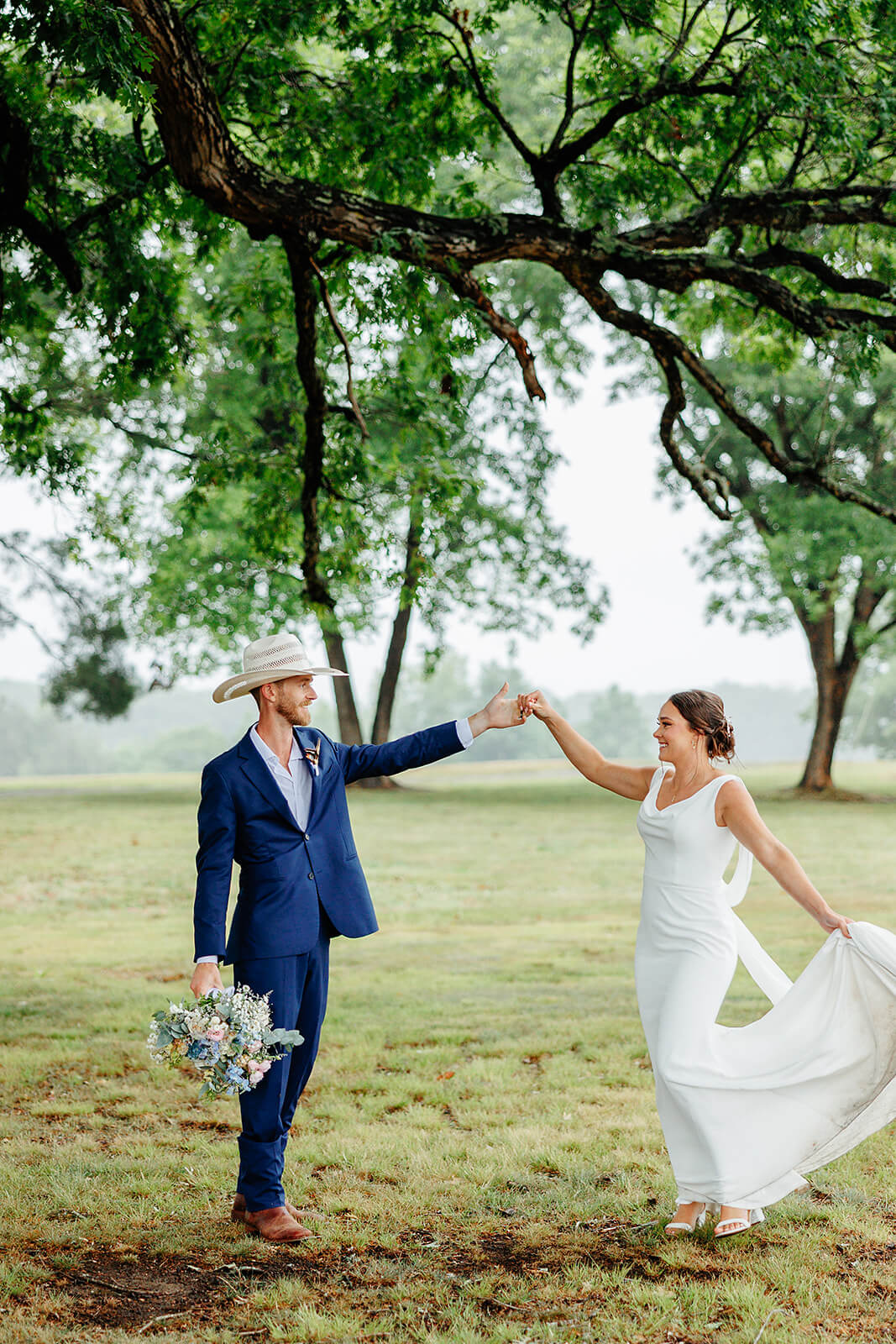 Family Farm Spring Wedding Photography 35 groom holding bride's hand and bouquet and twirling under a large tree