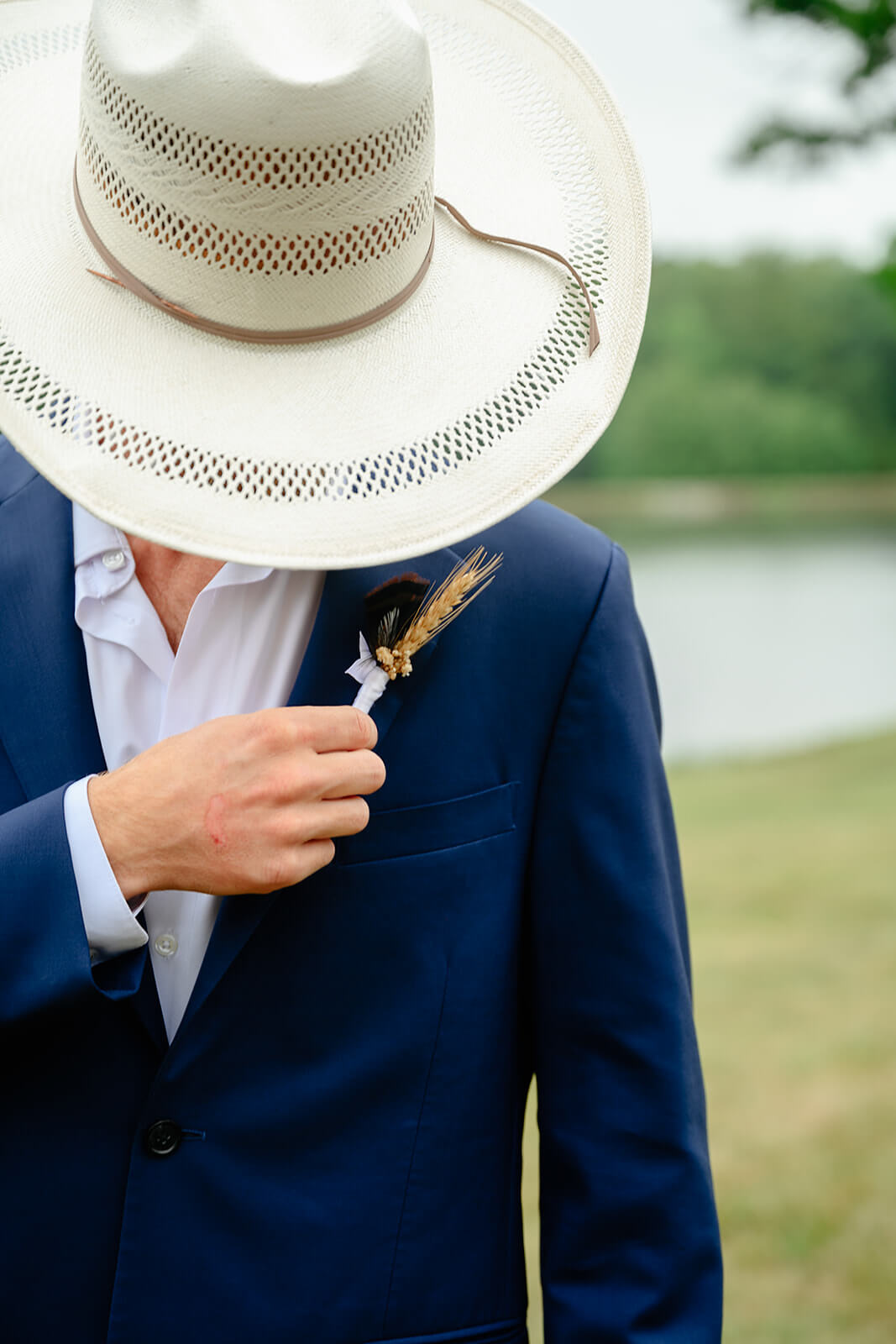 Family Farm Spring Wedding Photography 4 groom in farmers hat and navy jacket adjusting his wheat stalk in his bottom hole