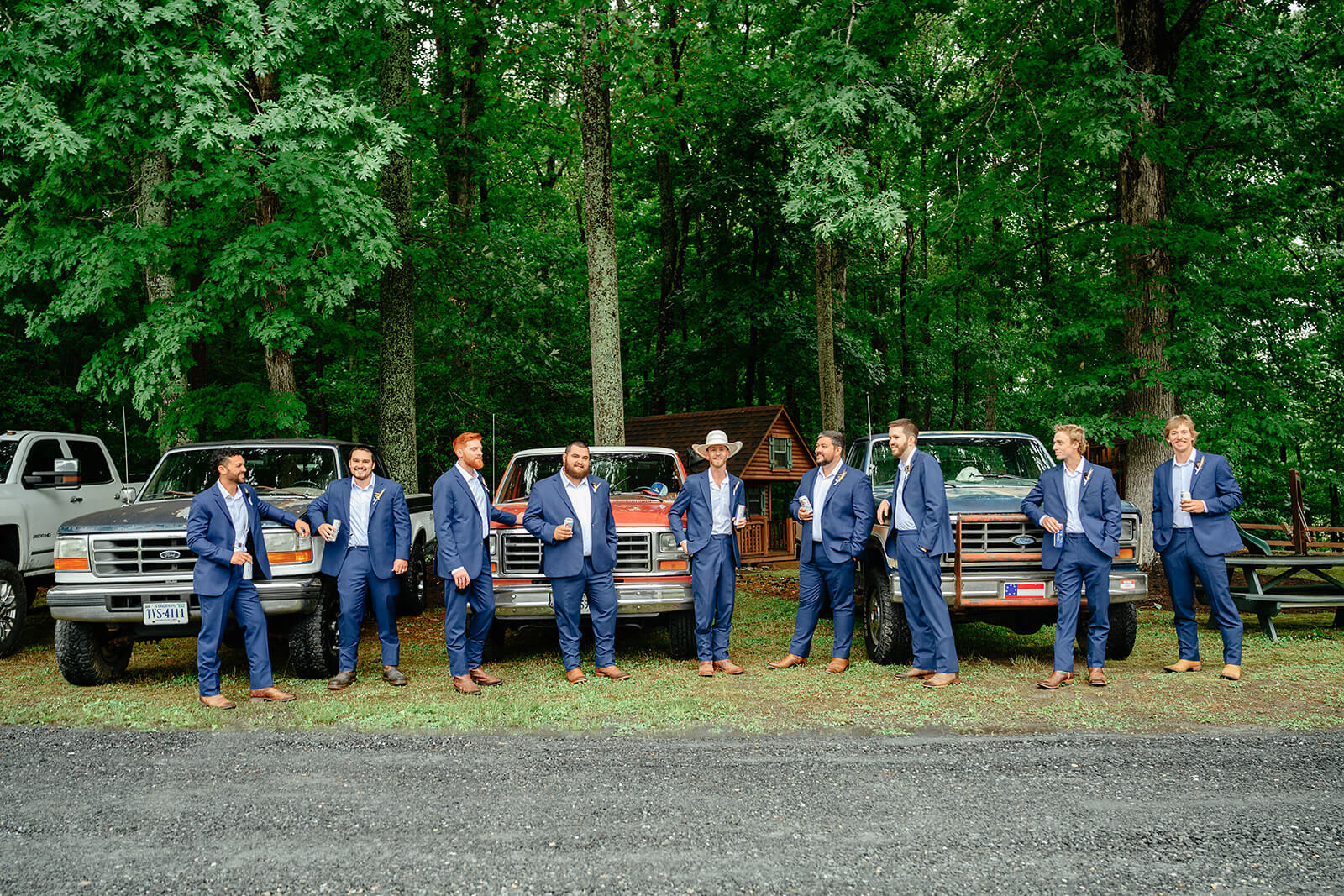 Family Farm Spring Wedding Photography 5 groom and groomsmen standing in front of three antique trucks holding beers