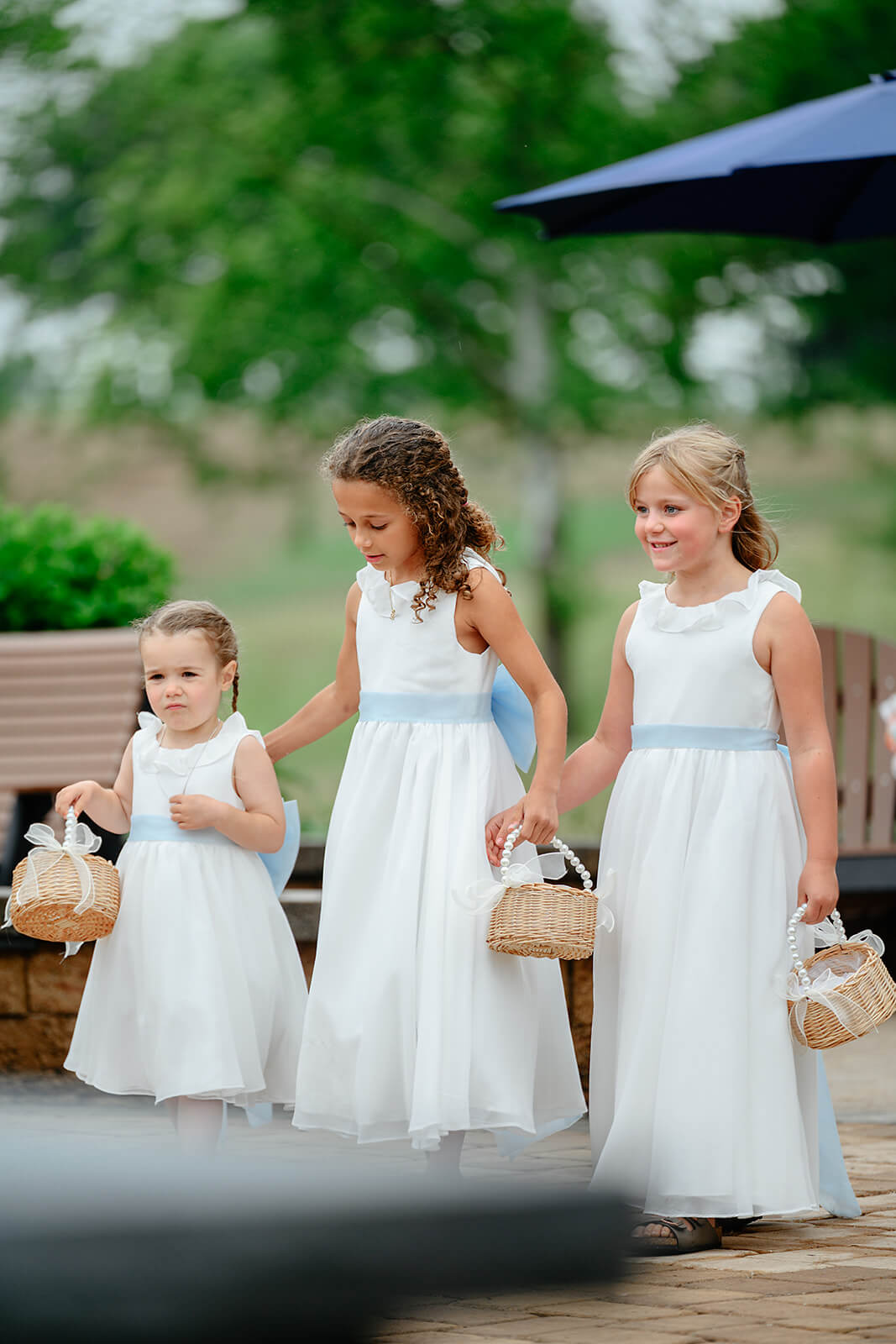 Family Farm Spring Wedding Photography 19 three young flower girls in white dresses with blue sashes carrying little wicker baskets