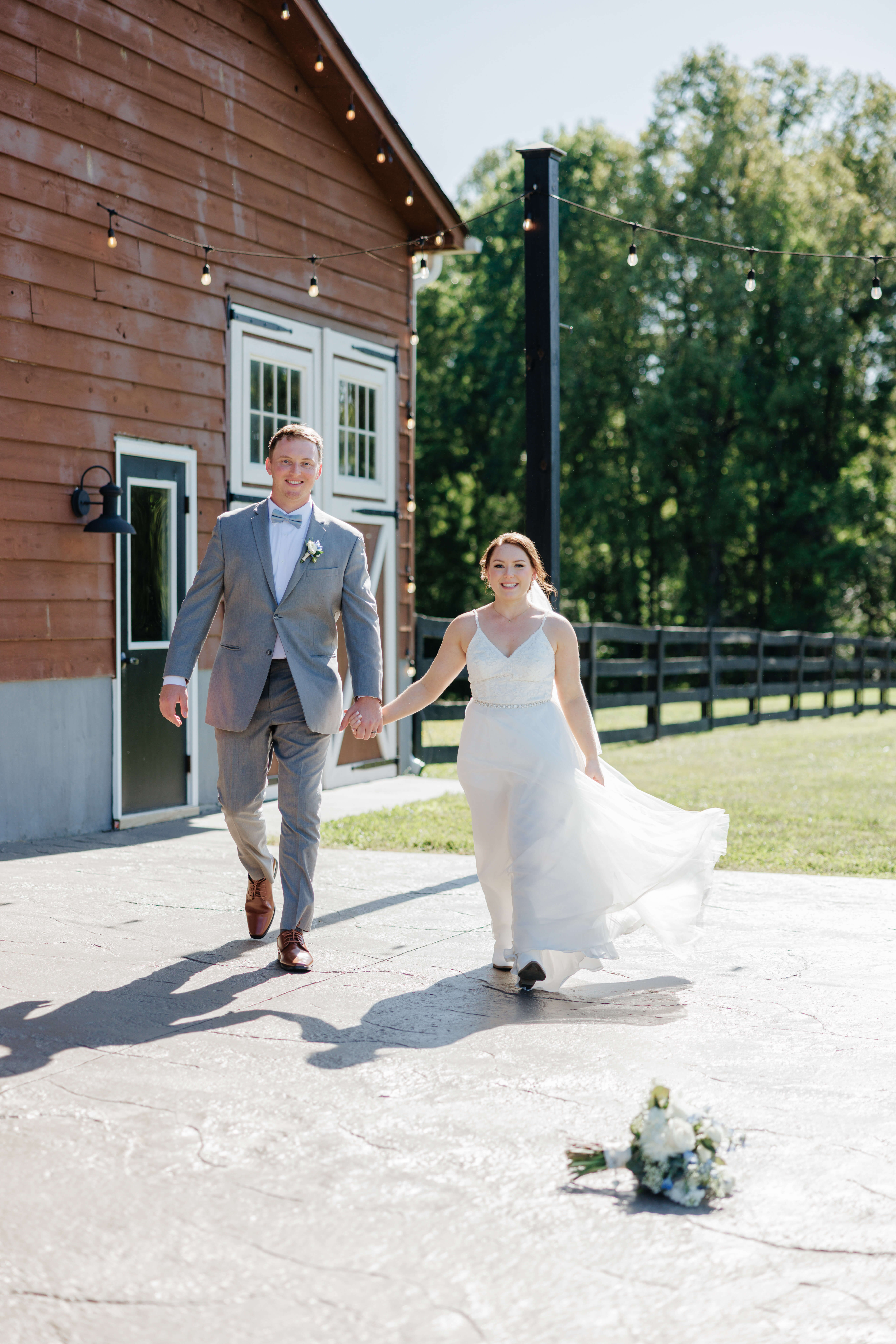 Malden Hill Spring Wedding Photography 19 bride and groom holding hands and walking, the brides bouquet is on the ground and there is barn behind them