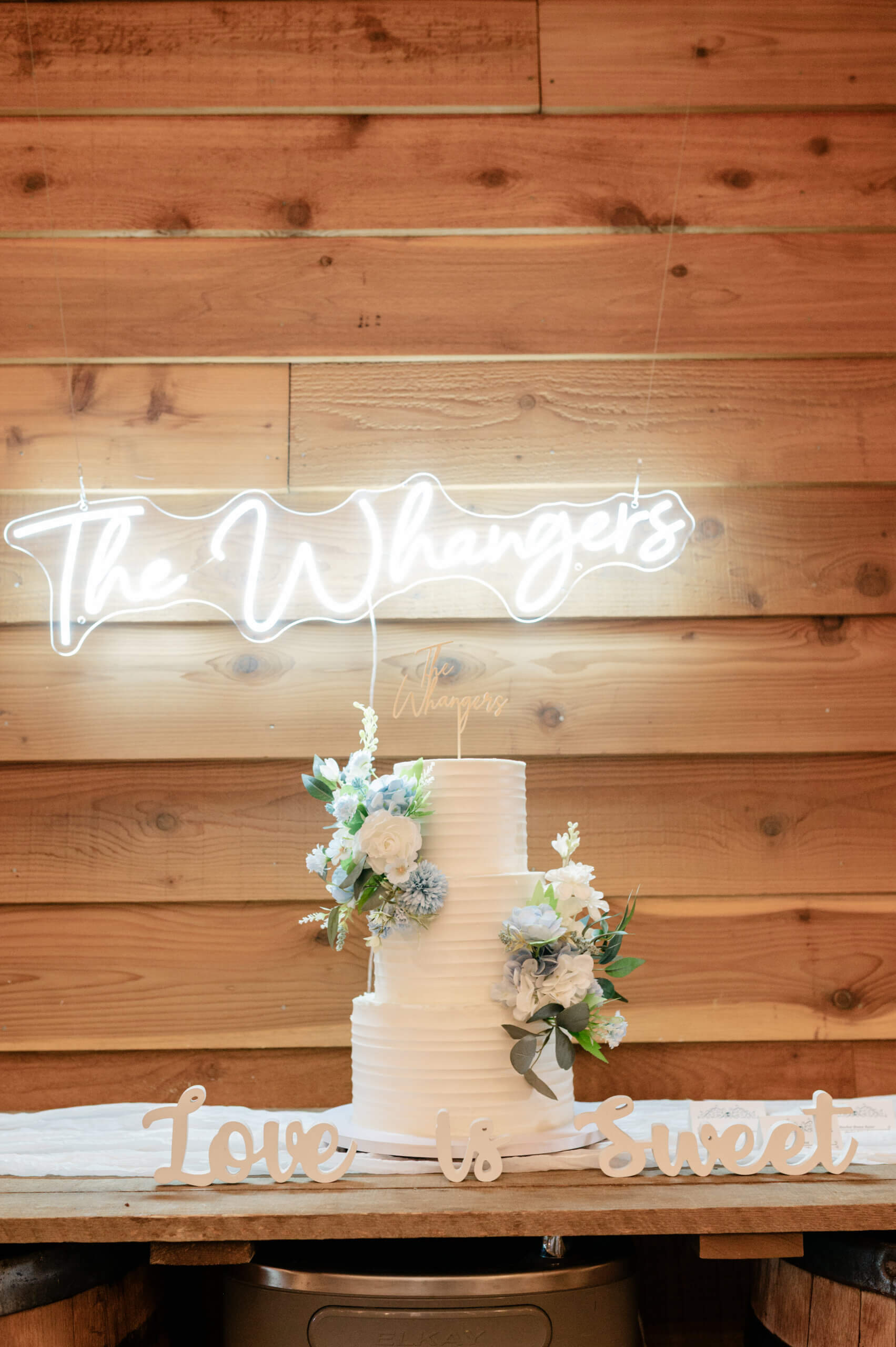 Malden Hill Spring Wedding Photography 21 detail photo of wedding cake with blue and white florals and couples name on a light up sign behind the cake