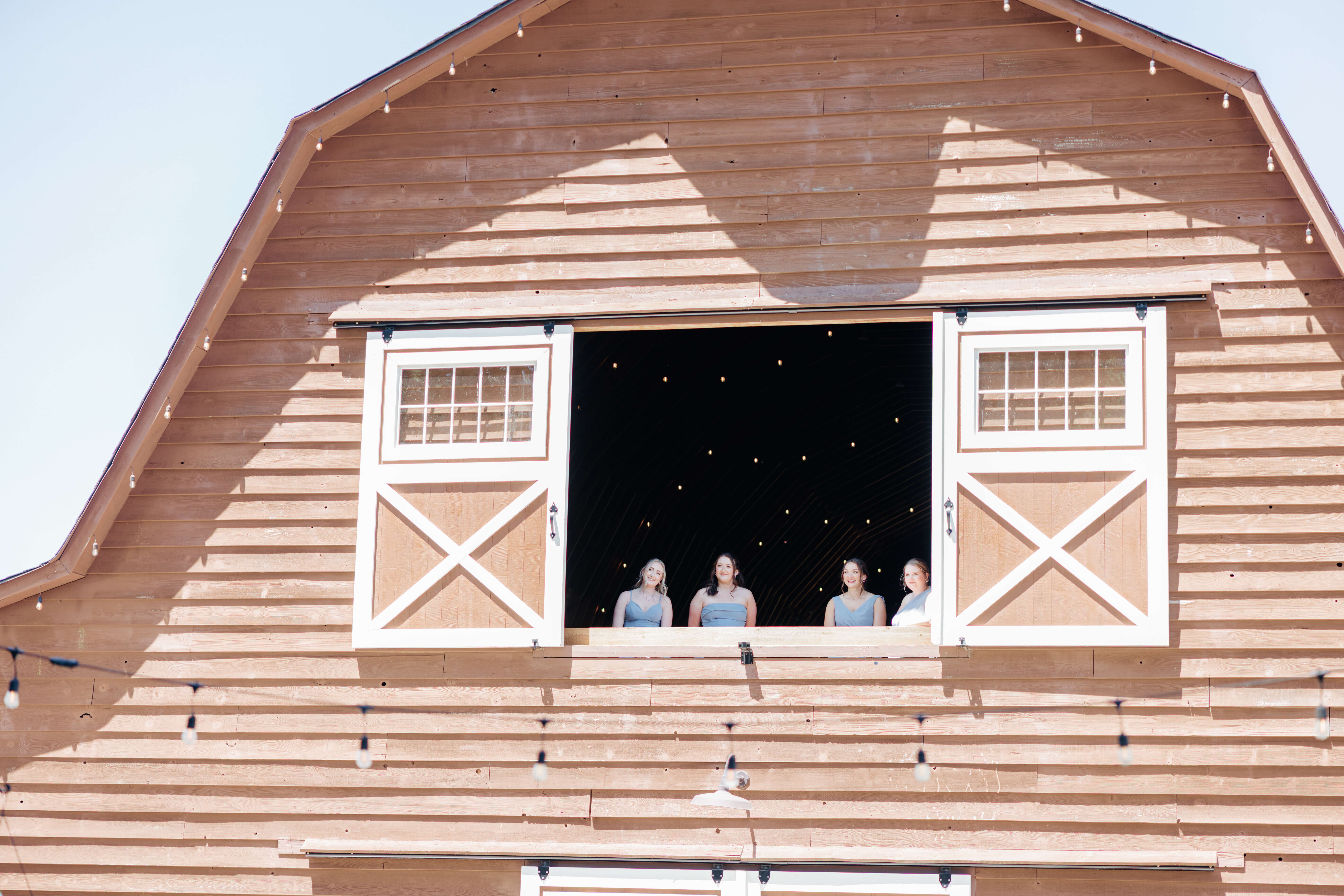 Malden Hill Spring Wedding Photography 8 bridesmaids watching out big barn window with twinkle lights above them