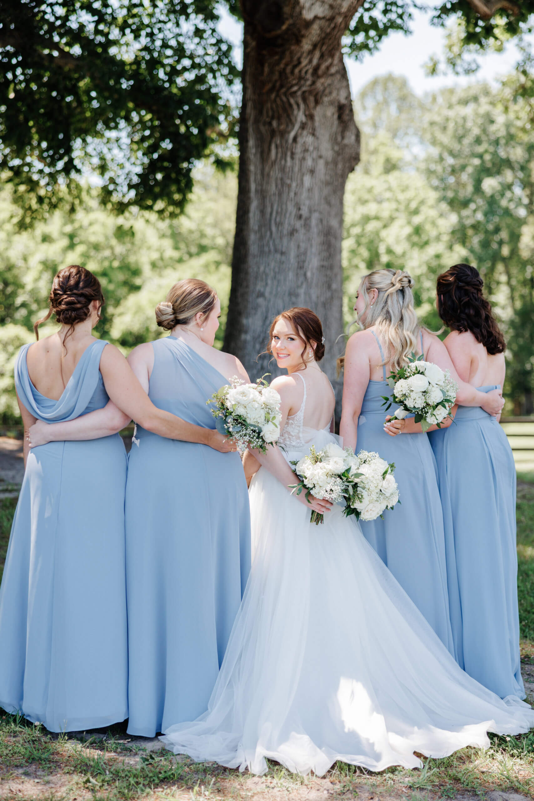 Malden Hill Spring Wedding Photography 9 bride and bridesmaids facing away from camera, holding eachothers backs, bride is turned around and smiling at camera