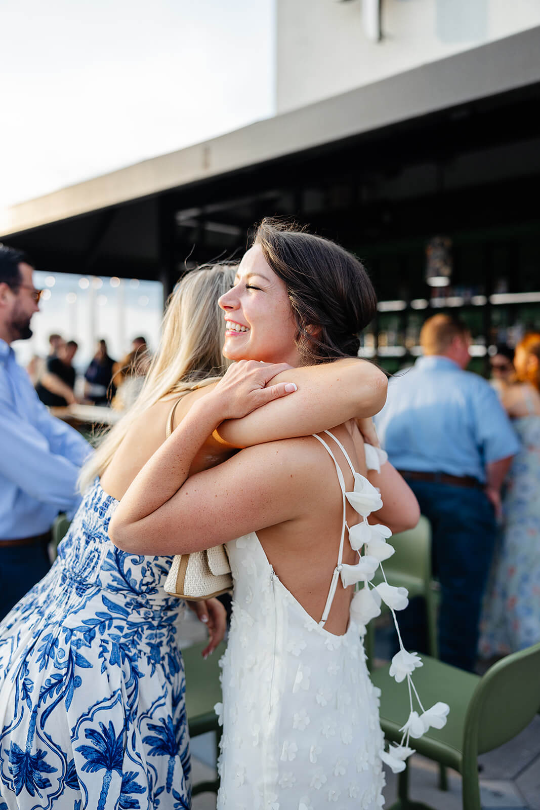 Estate at River Run Summer Wedding Photography 2 bride in white flowy dress hugging guests on a rooftop bar