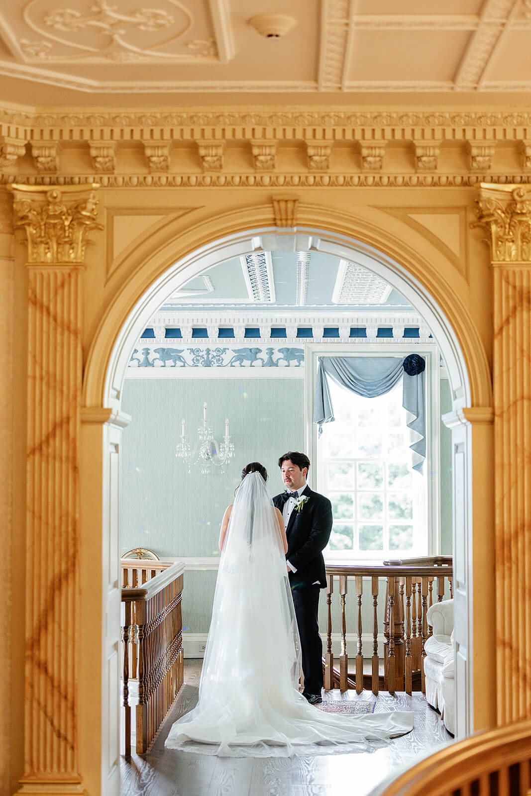 Estate at River Run Summer Wedding Photography 14 bride and groom holding hands in a hallway with a golden wall and archway in the foreground