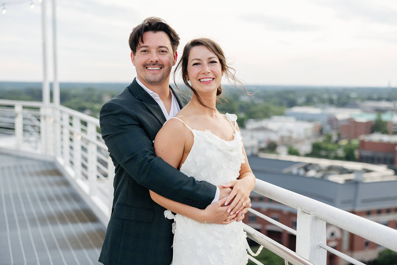Estate at River Run Summer Wedding Photography 4 portrait of bride and groom on deck of downtown building, they are facing the camera and he is hugging her from behind