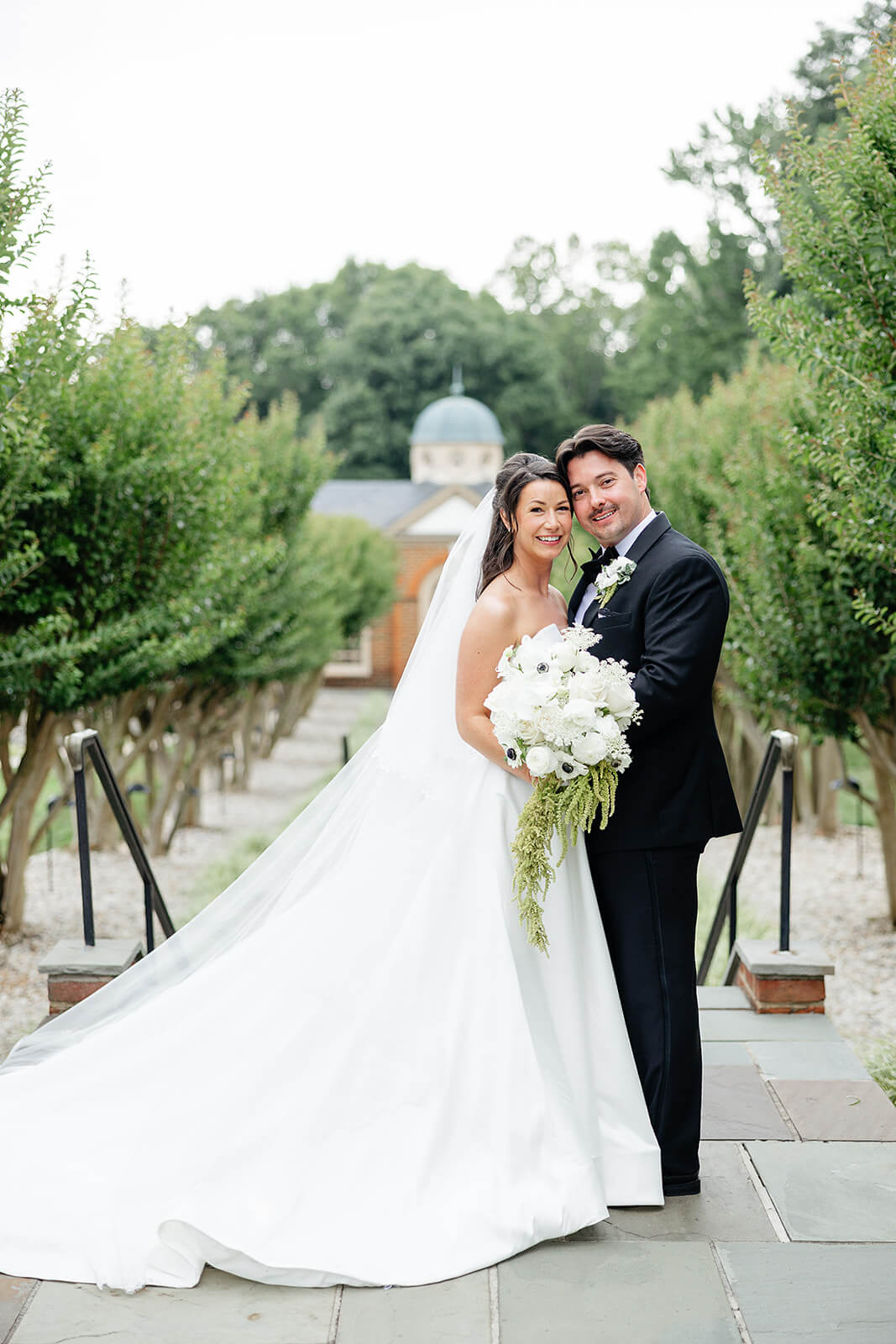 Estate at River Run Summer Wedding Photography 19 portrait of bride and groom standing on a stone path with lines of trees on either side of them