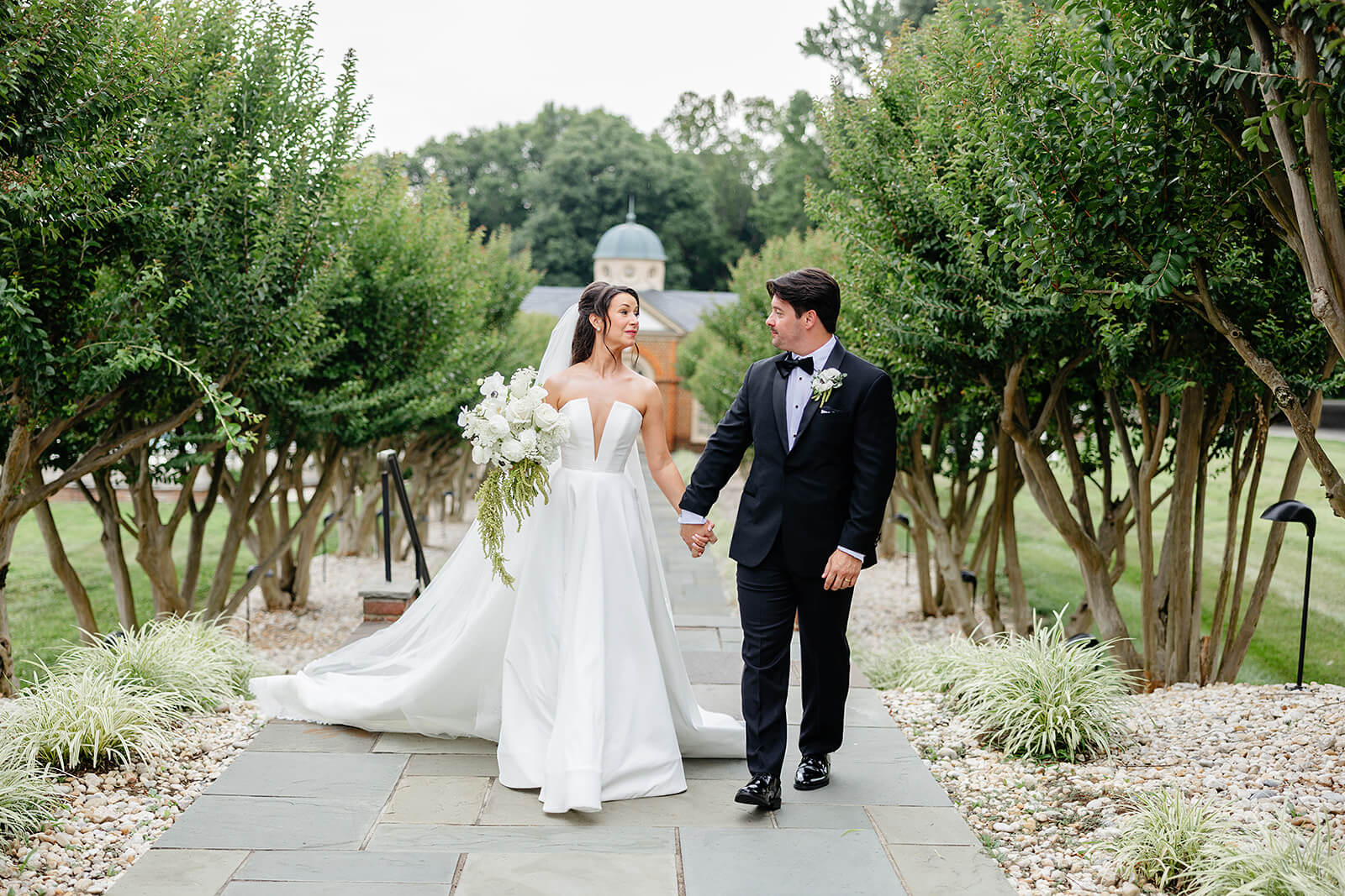 Estate at River Run Summer Wedding Photography 21 bride and groom holding hands and walking down a stone path between crepe myrtle trees