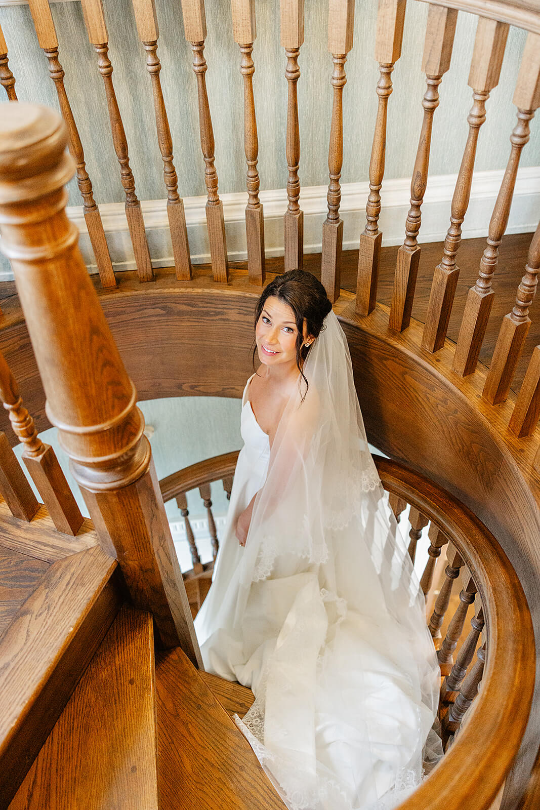 Estate at River Run Summer Wedding Photography 27 bride looking at the camera as she walks down a wooden spiral staircase