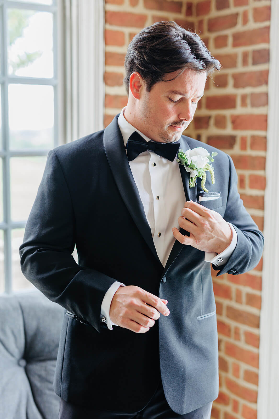 Estate at River Run Summer Wedding Photography 8 groom standing against brick wall looking at his boutonniere