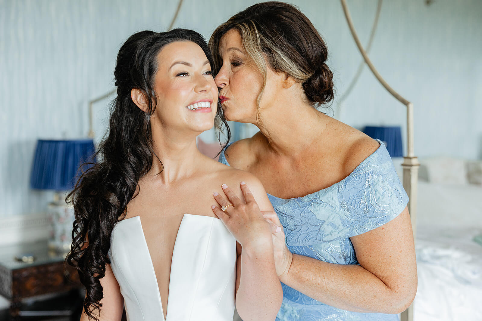 Estate at River Run Summer Wedding Photography 10 bride in her wedding dress getting kissed on the cheek by her mom in a blue, off the shoulder dress