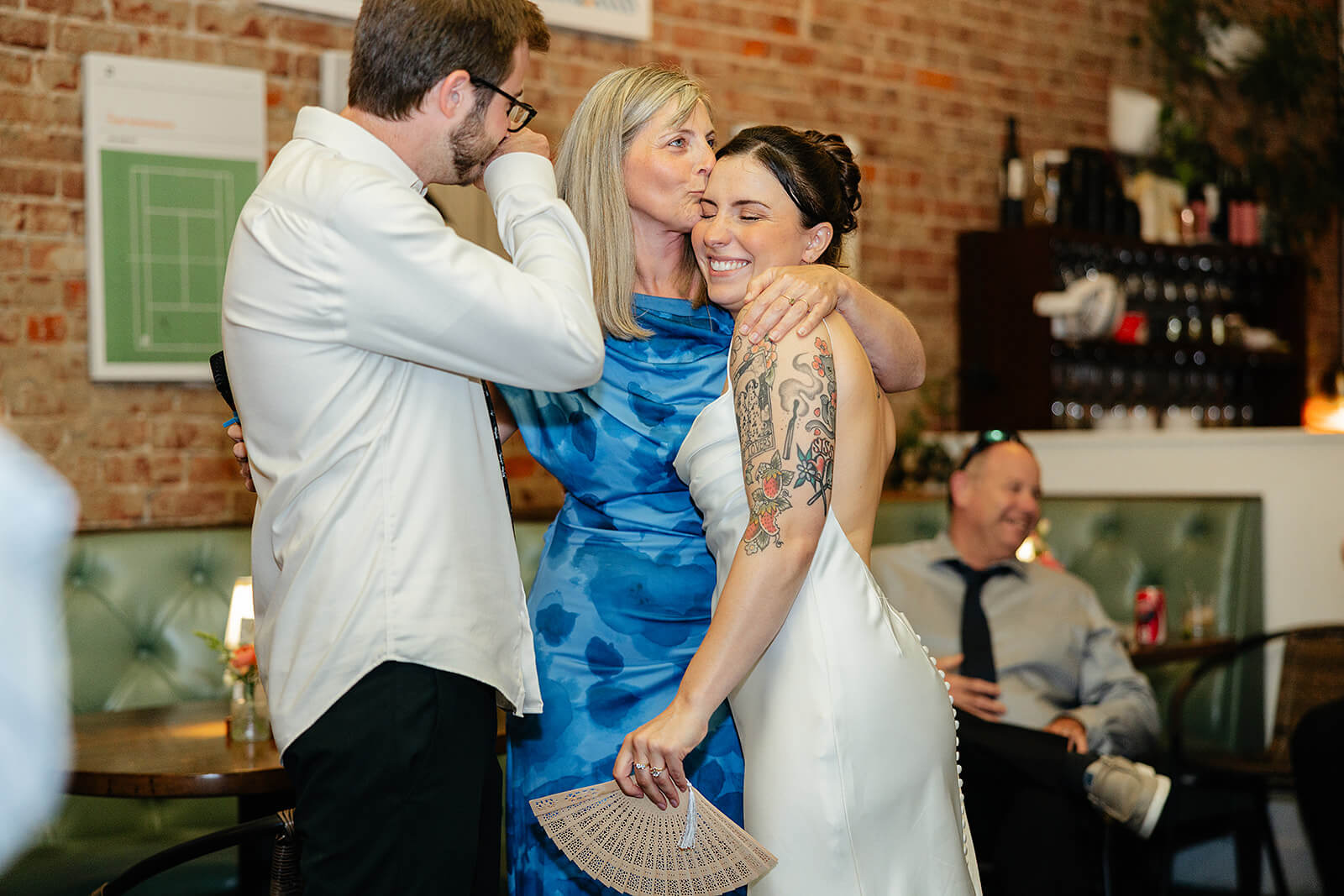 Laura Lee's Spring Wedding Photography 30 bride and groom getting a hug and kiss from a guest in a bright blue dress