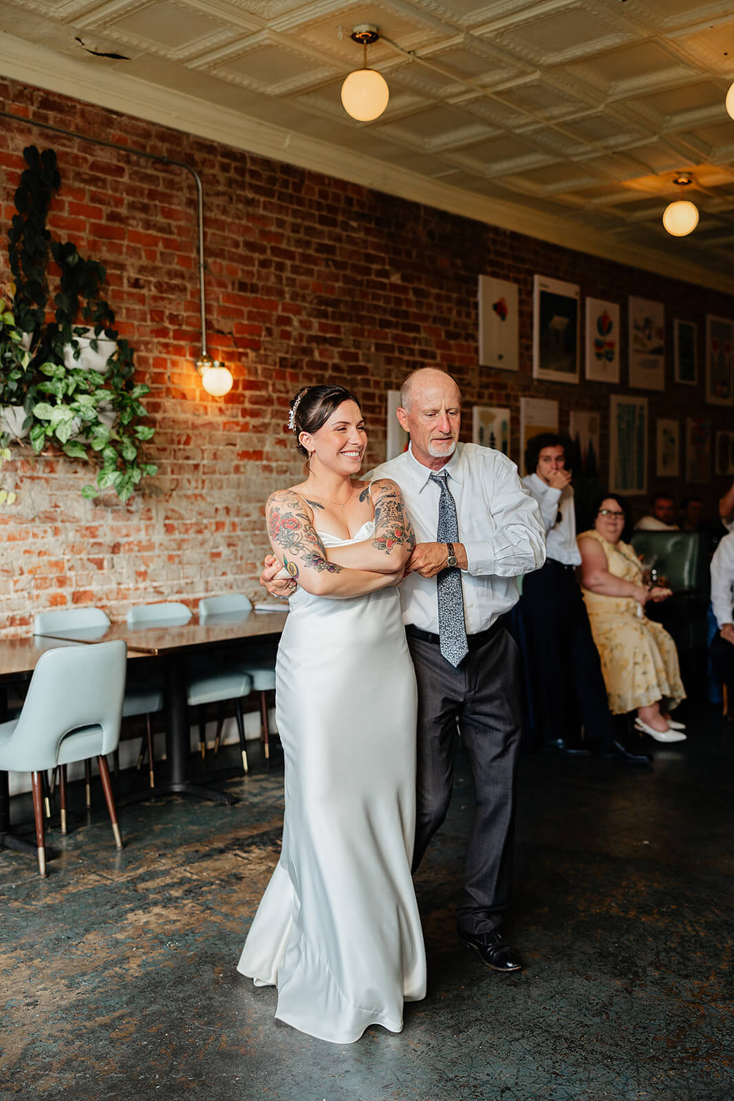 Laura Lee's Spring Wedding Photography 21 bride dancing with her dad on concrete floor with brick wall and industrial lighting around them