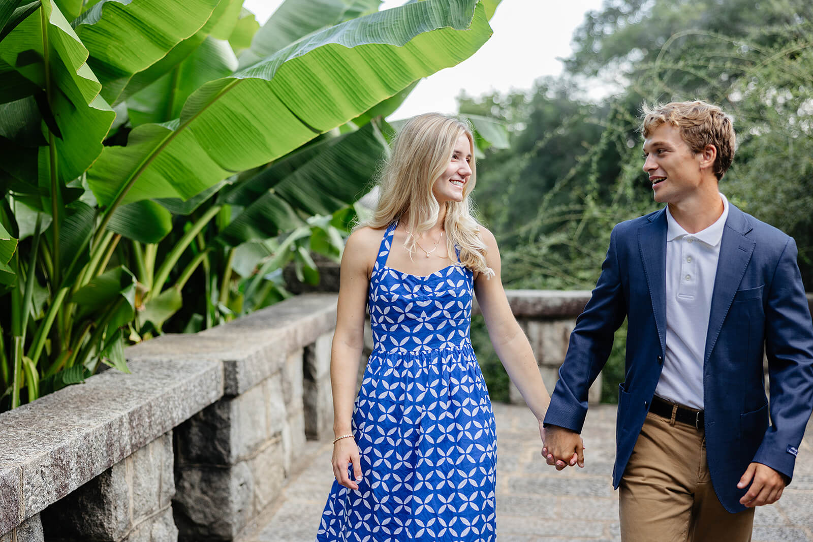 Maymont Summer Engagement Photography 1 couple holding hands walking on stone balcony with large leaves hanging onto the railing