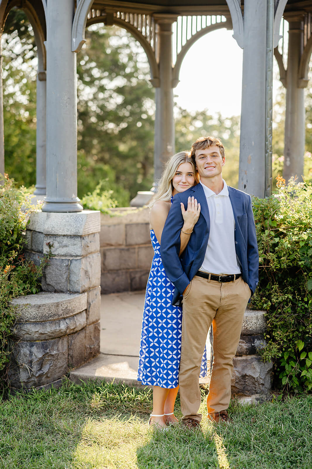 Maymont Summer Engagement Photography 14 woman hugging her fiance from behind as they stand in front of a gazebo with stone accents
