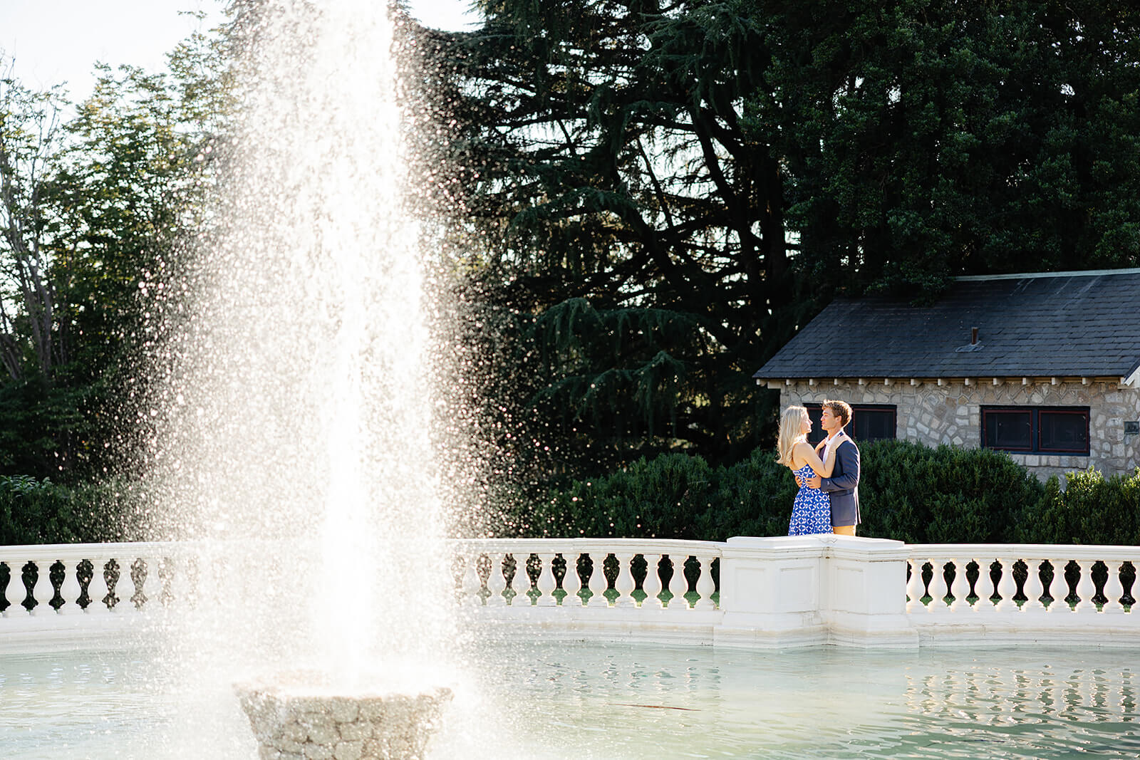 Maymont Summer Engagement Photography 18 couple hugging each other in the background with a huge fountain is spraying the foreground