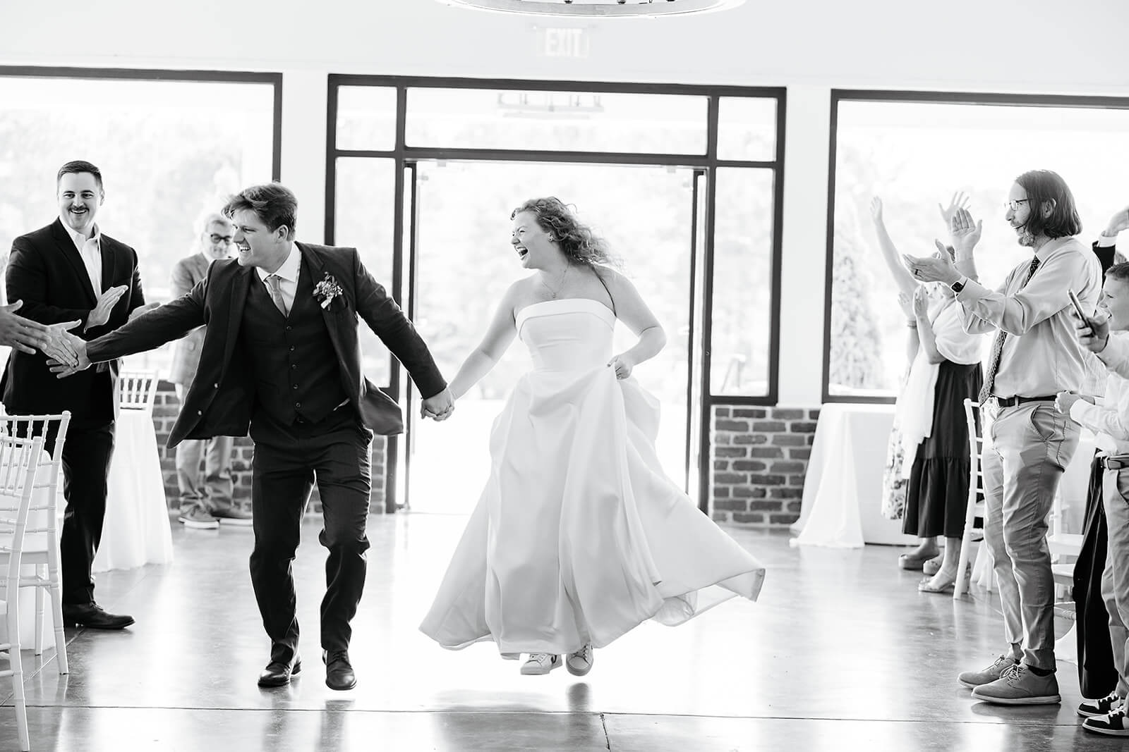 Rassawek Vineyard Spring Wedding Photography 33 black and white photo of bride and groom holding hands and running into reception, all the guests are standing and cheering for them