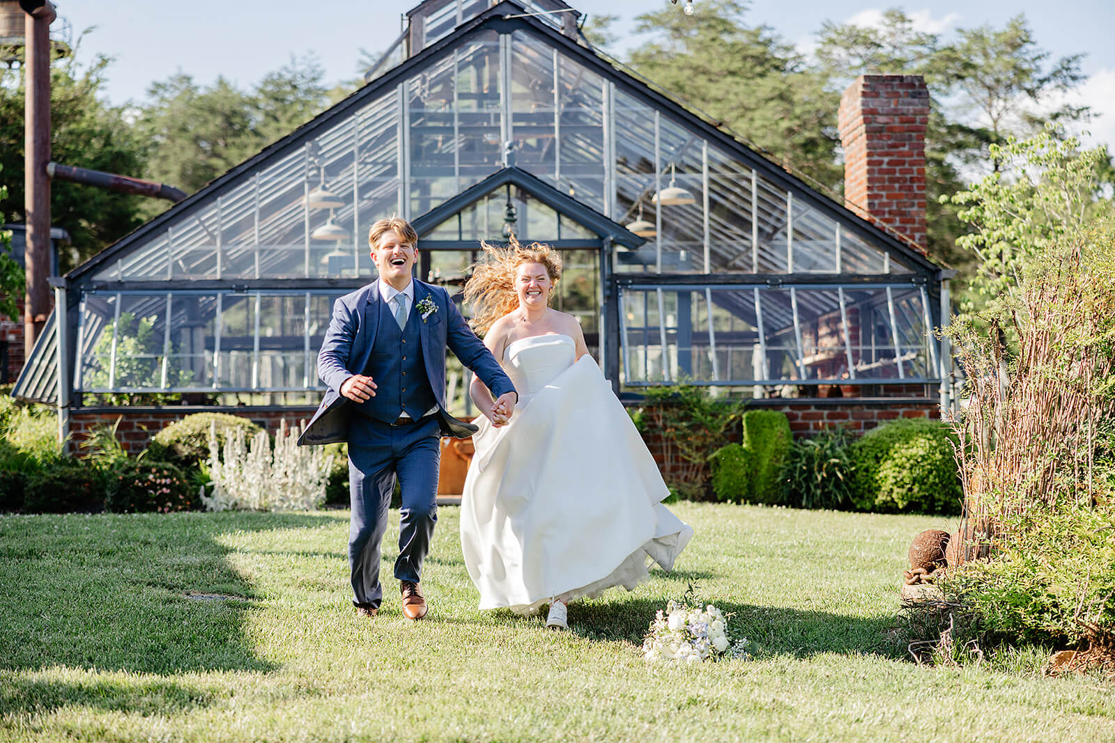 Rassawek Vineyard Spring Wedding Photography 26 bride and groom running through the lawn in front of greenhouse made of glass windows and brick