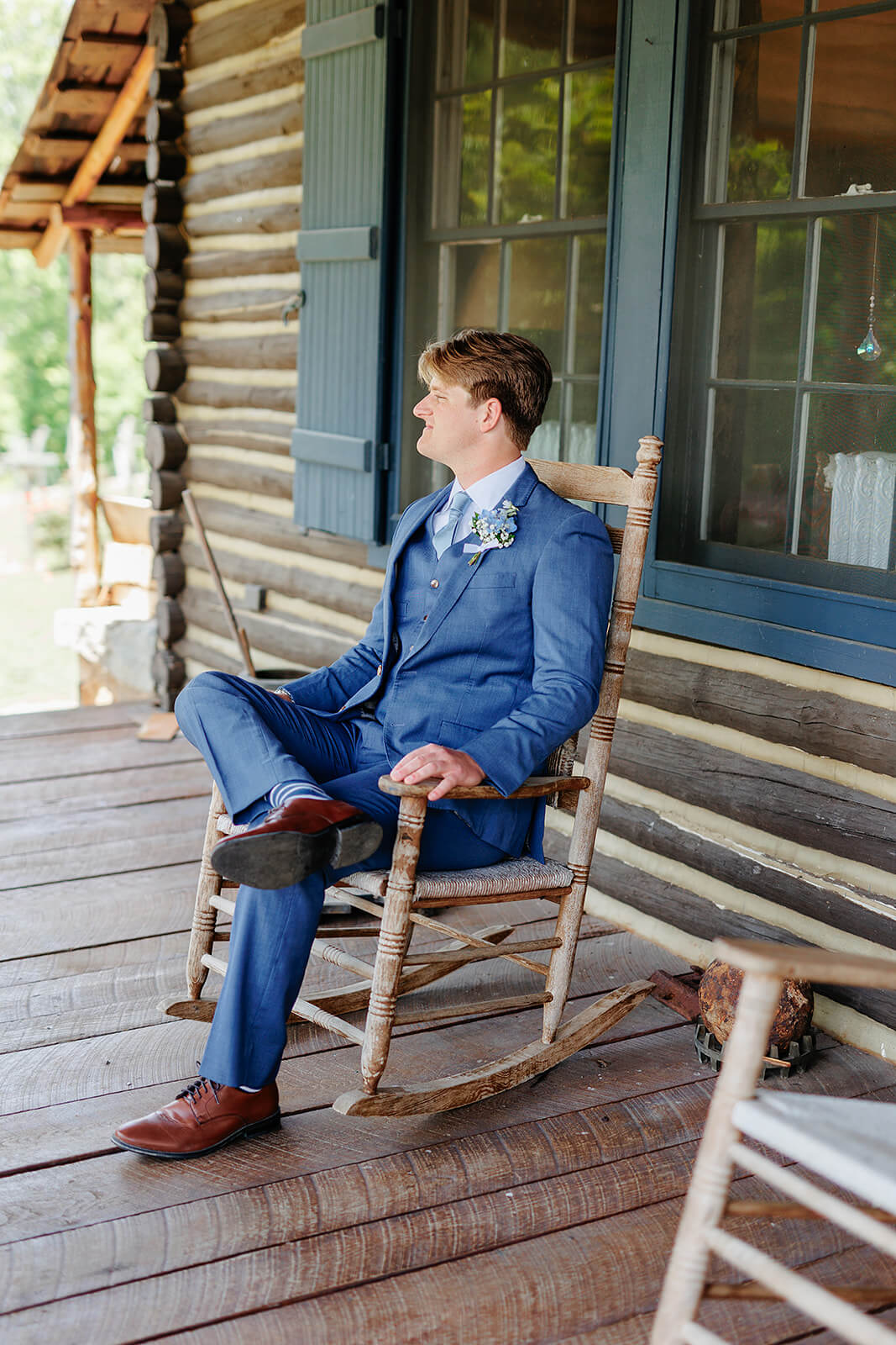 Rassawek Vineyard Spring Wedding Photography 1 groom in navy suit sitting on wooden rocking chair on cabin porch