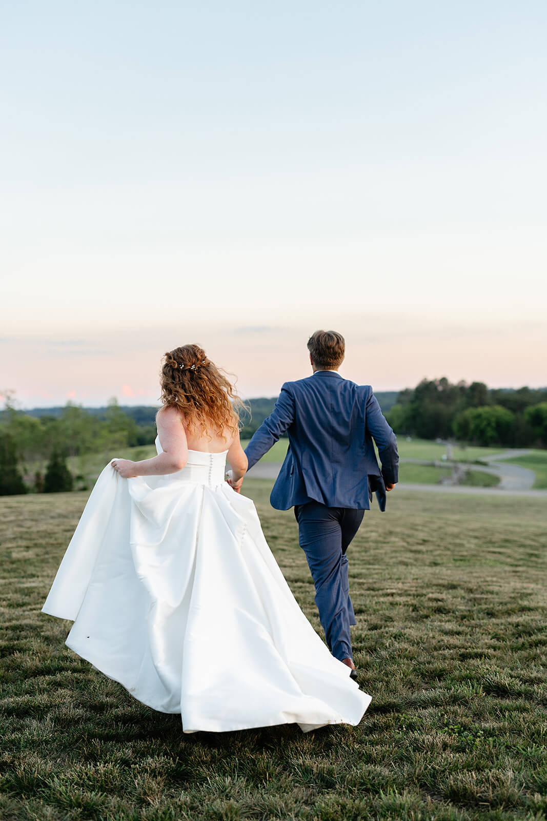 Rassawek Vineyard Spring Wedding Photography 48 bride and groom holding hands and walking away from the camera across a long hilly yard