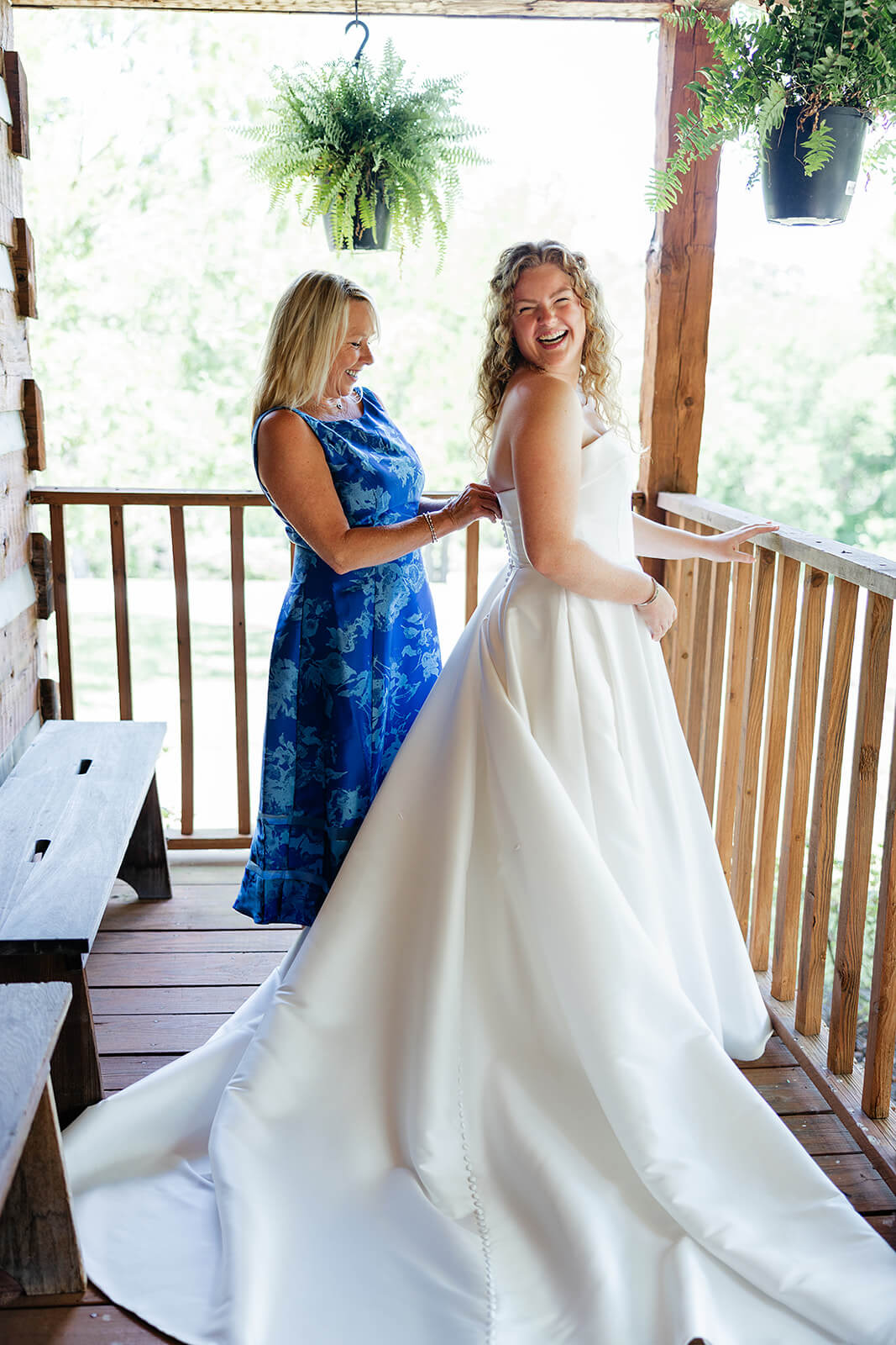 Rassawek Vineyard Spring Wedding Photography 5 bride in her dress standing on wooden porch with her mom in a blue dress zipping brides dress