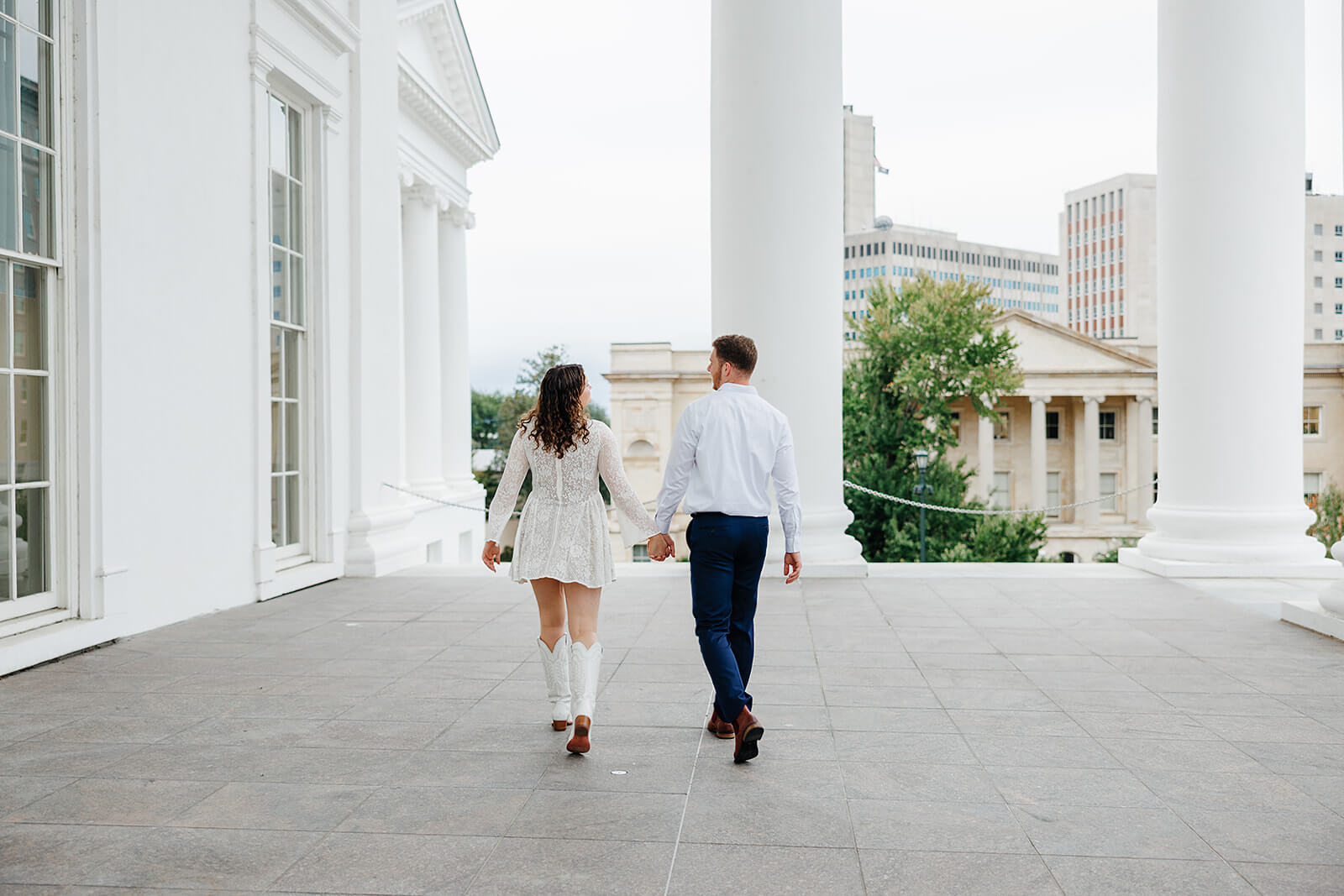Virginia Capital Fall Engagement Photography 1 couple holding hands and walking on large porch with white columns around it. they are walking away from the camera