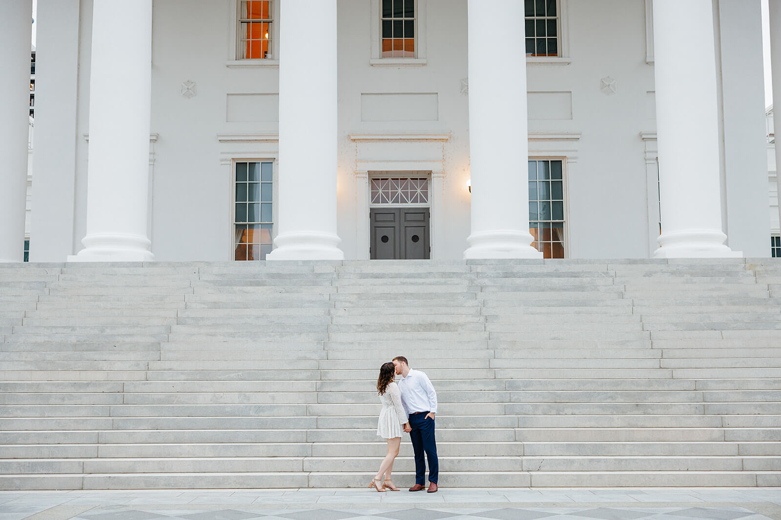 Virginia Capital Fall Engagement Photography 10 couple kissing at the bottom of large white stairs that lead up to big porch with large white columns lining the porch