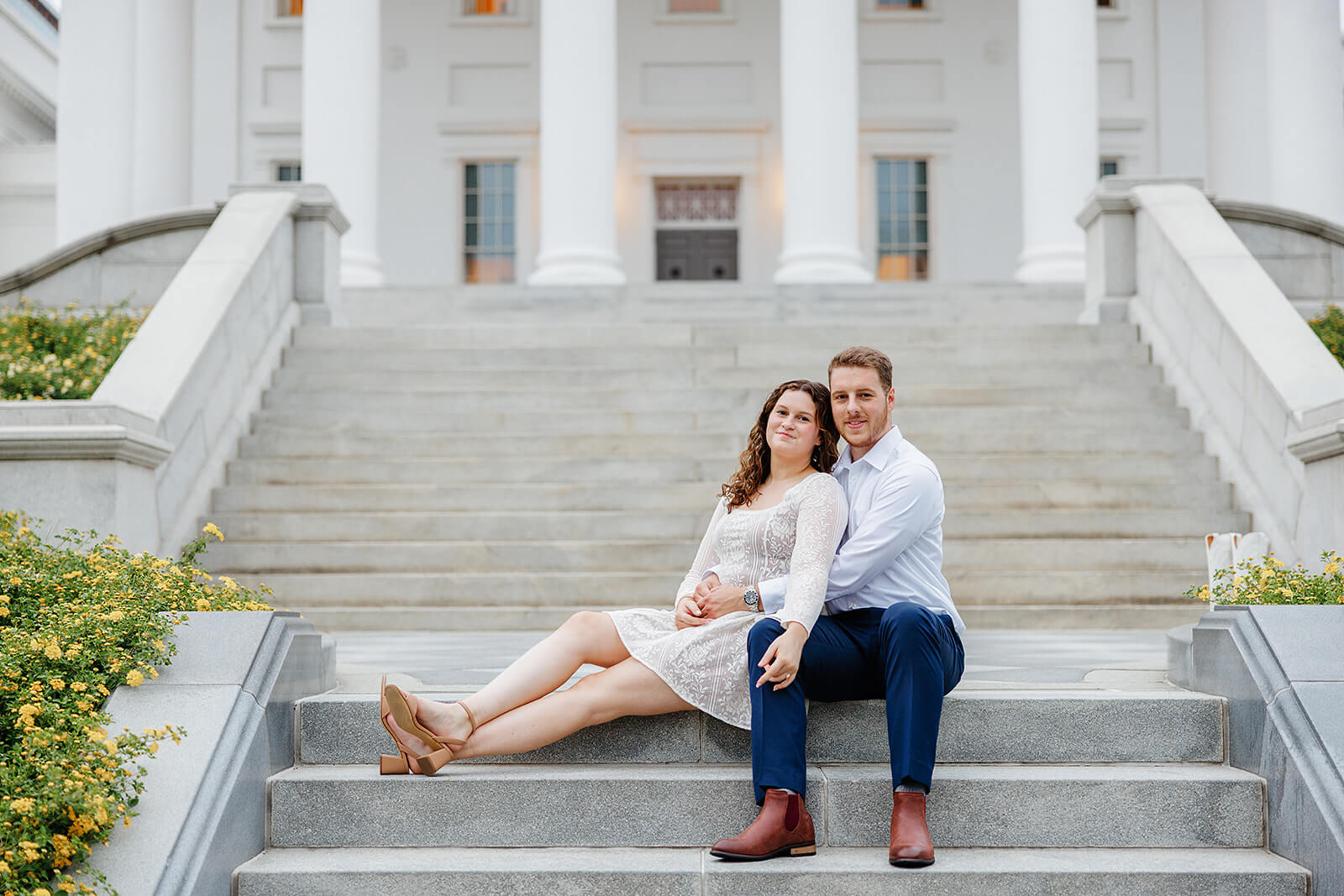 Virginia Capital Fall Engagement Photography 15 couple sitting on stairs in front of large porch, he is hugging her and she sits next to him with her legs stretched out