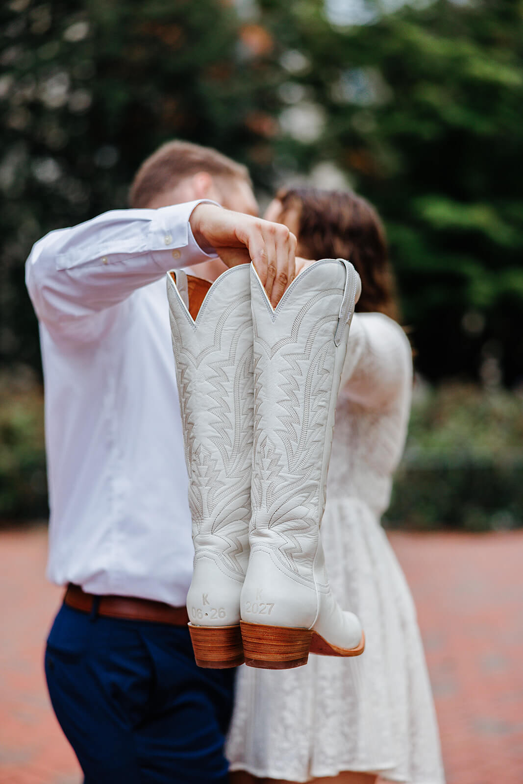 Virginia Capital Fall Engagement Photography 18 couple kissing in the background while they hold a pair of white boots in front of their faces
