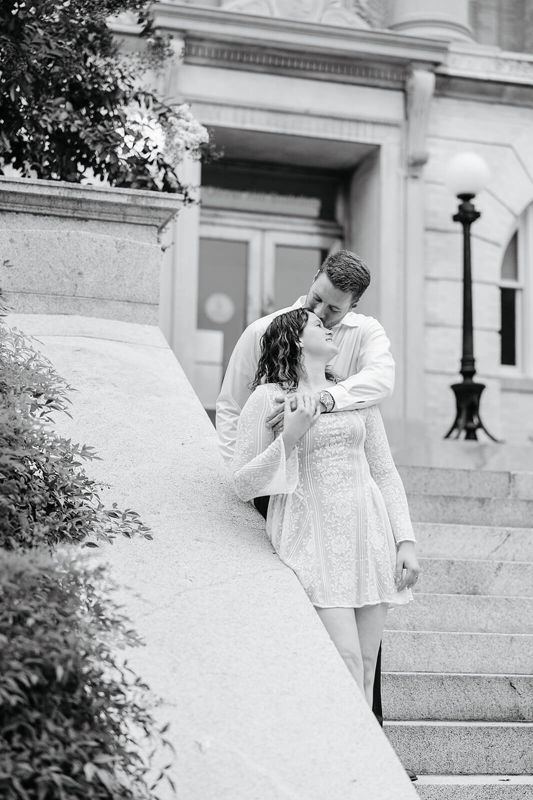 Virginia Capital Fall Engagement Photography 19 black and white photo of couple standing on stone staircase, her head is leaned back and he is kissing her forehead