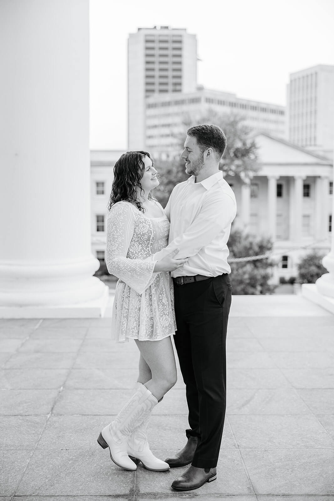 Virginia Capital Fall Engagement Photography 4 black and white photo of couple holding each other and smiling at each other. they are outside on large porch with big buildings in the background
